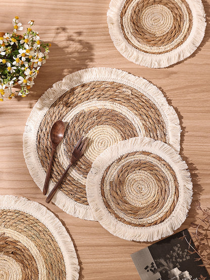 Woven placemats with fringes on a wooden table with a spoon and fork.