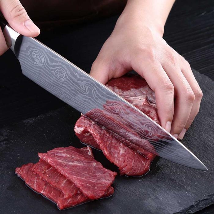 Person slicing raw beef with a chef's knife on a dark surface