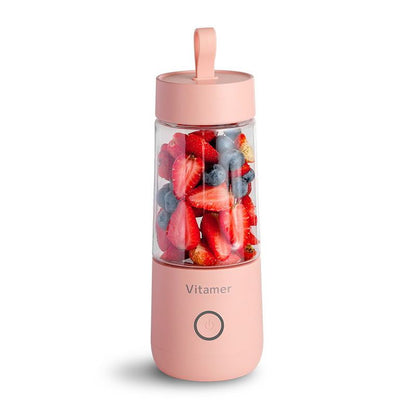 Portable blender with pink body and clear lid filled with fruits on a white background