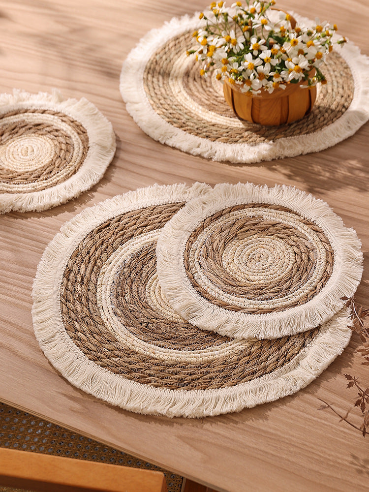 Set of woven placemats with fringe on a wooden table.