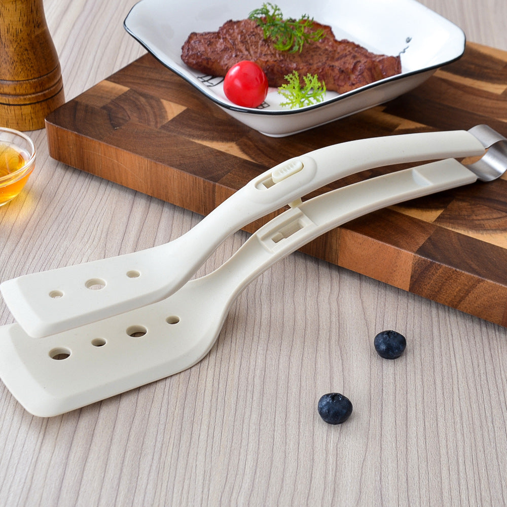 White kitchen tongs on a wooden surface with a plate of food in the background