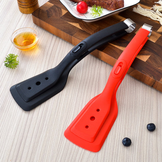 Two spatulas, one black and one red, on a wooden cutting board with food items in the background.