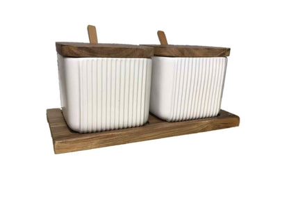 Two white ceramic containers with wooden lids on a wooden tray against a white background