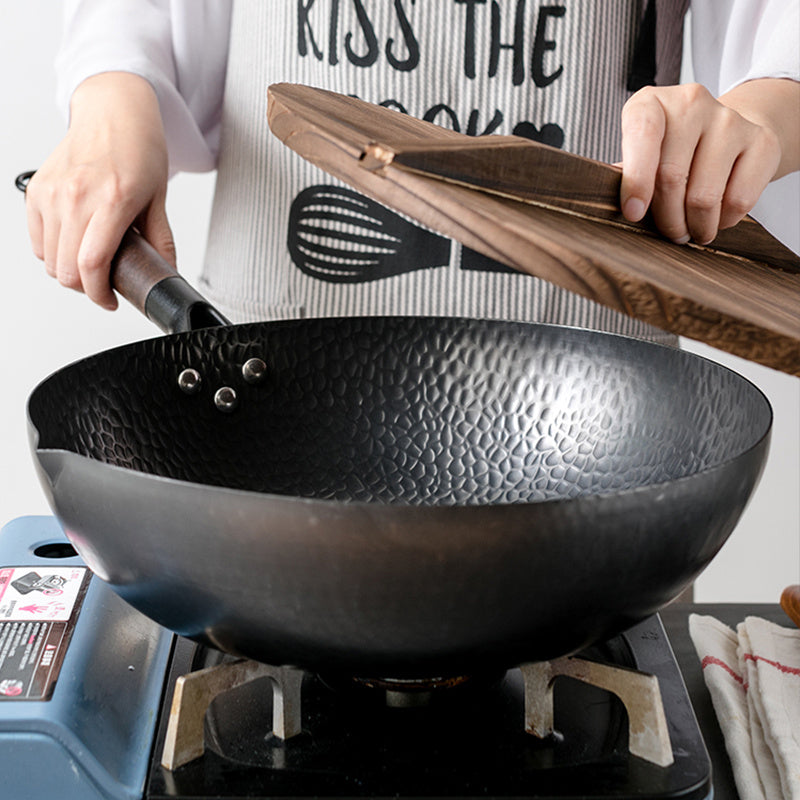 Person holding a wooden spatula over a black wok on a stove