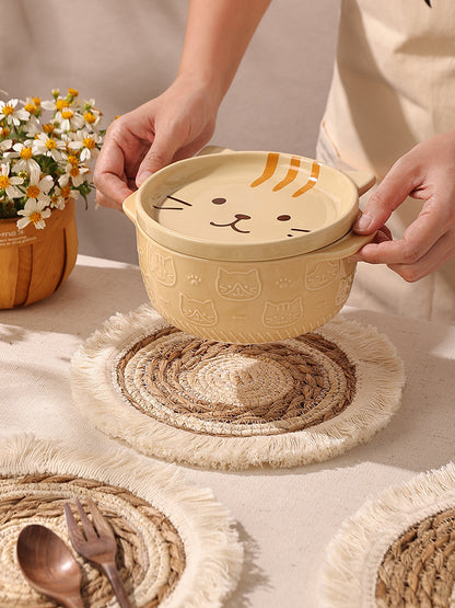 Beige ceramic bowl with cat design held by a person on a textured surface with flowers and cutlery.